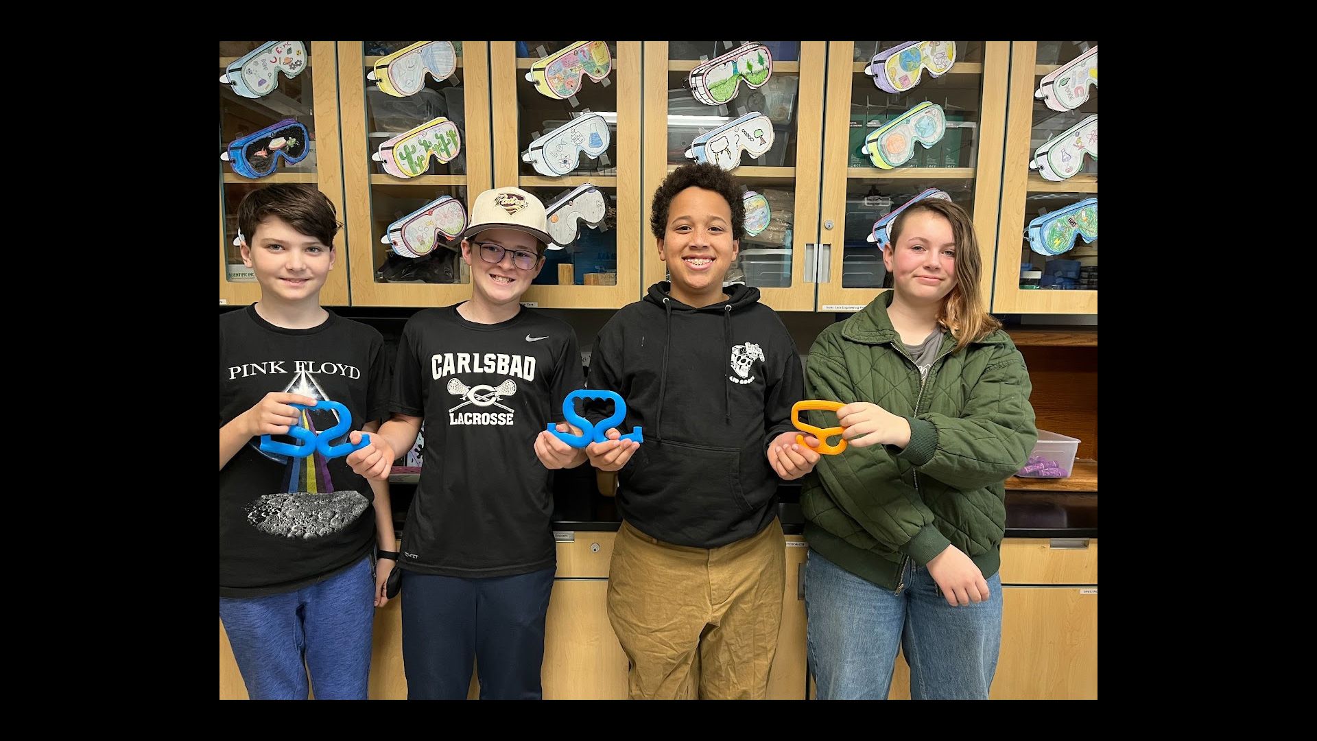 4 students holding up 3D printed assistive bag holders.
