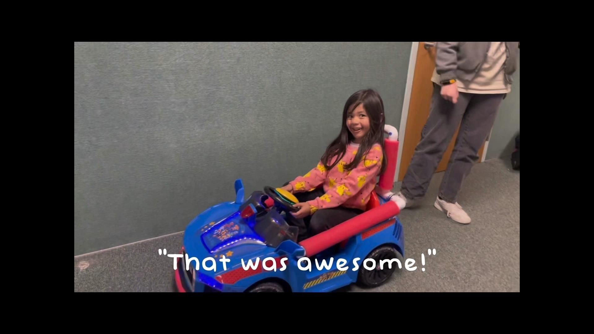 Student sat in an adaptive toy car with "That was awesome!" overlaid onto image.