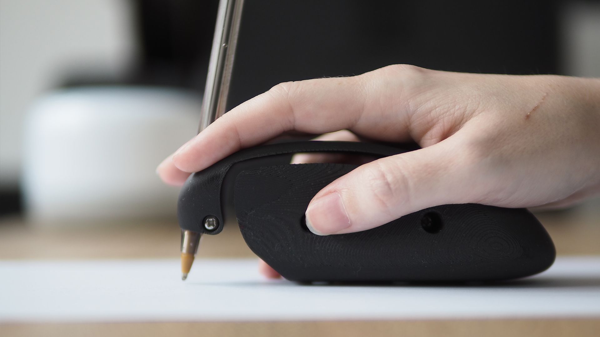 A hand using a 3D printed assistive writing/drawing device, shaped like a mouse.