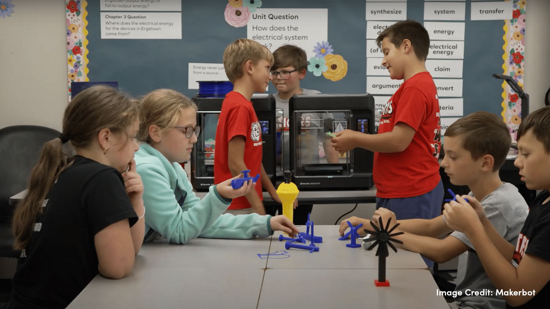 Students in a classroom with Makerbot 3D printers and 3D printed objects on a table.