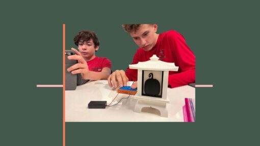 2 students sat at a desk with a lamp controlled by a 3d printed switch access device.