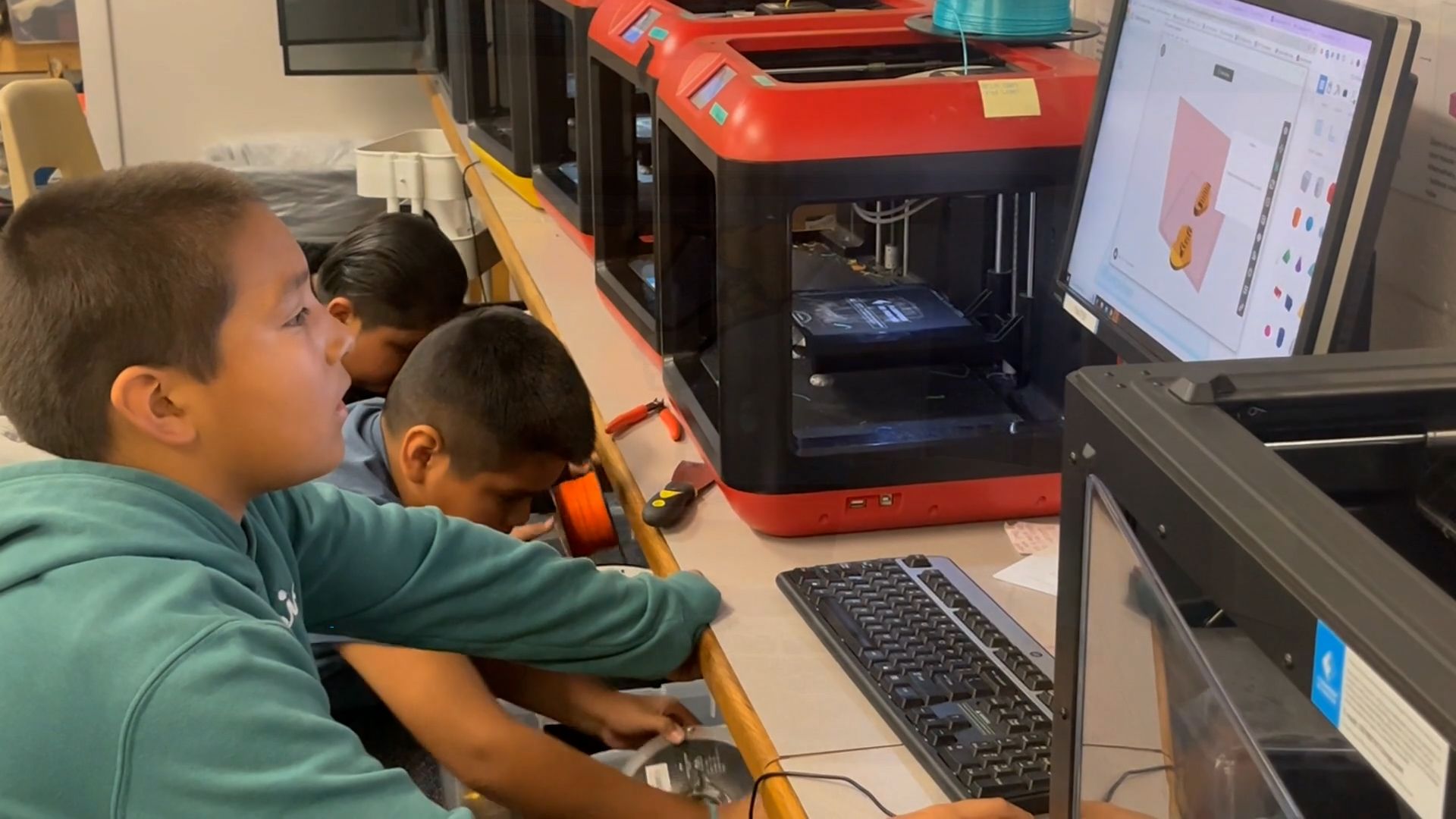 A student working on a design in Tinkercad next to a series of 3D printers.