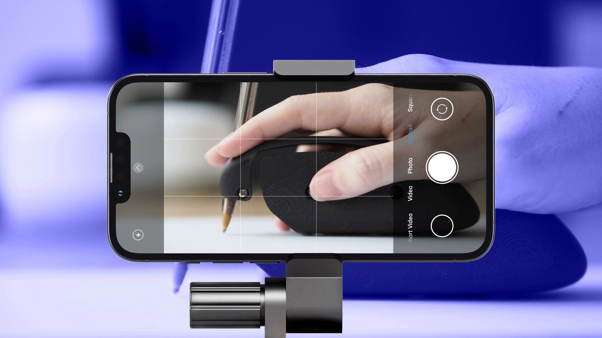A smartphone with the camera app open, taking a picture of the DRAG assistive writing aid.