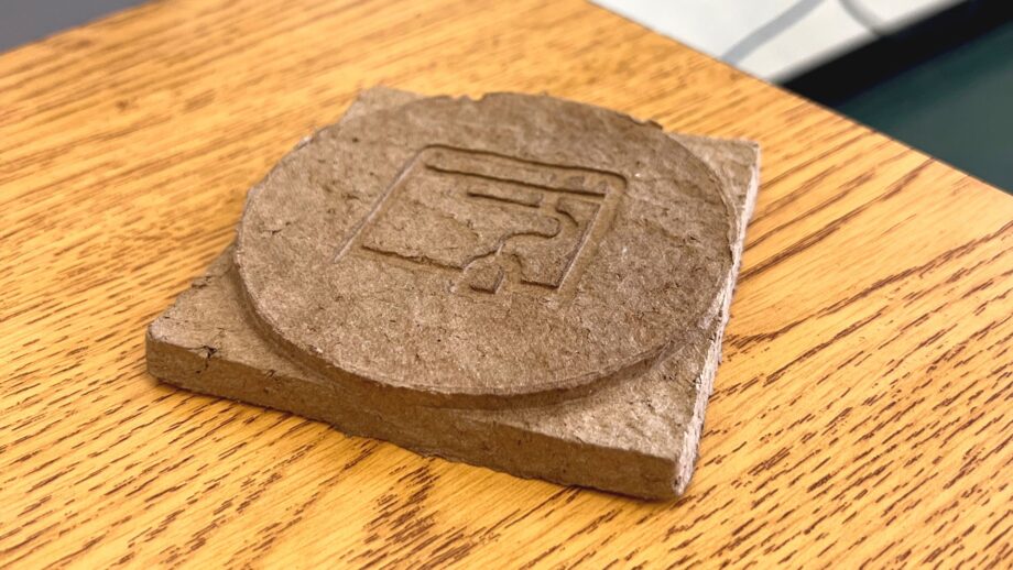 A finished recycled cardboard coaster with an embossed design, resting on a wooden surface.