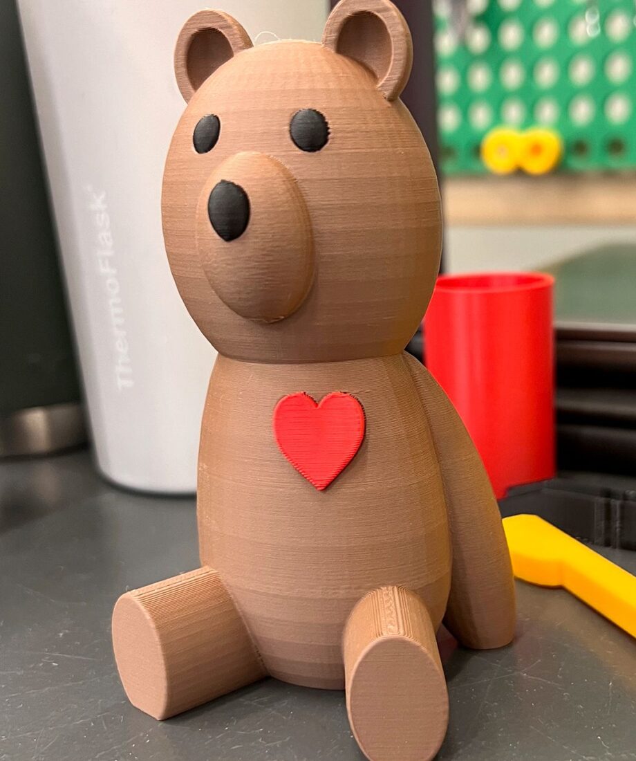 A 3D printed brown bear figurine sitting upright with black eyes and a red heart detail on its chest.