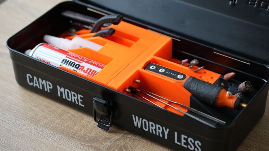 Orange 3D printed storage organiser inserts fitted inside a black toolbox, holding glue, pliers, rotary tool accessories, and hand tools in custom cut compartments.