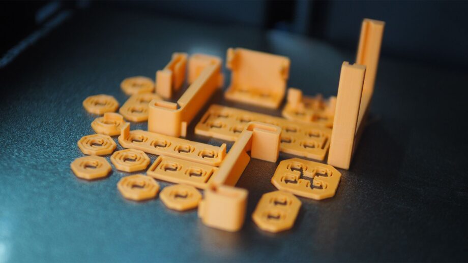 Close-up photo of orange 3D printed MakerTrack base kit parts laid out on a print bed.