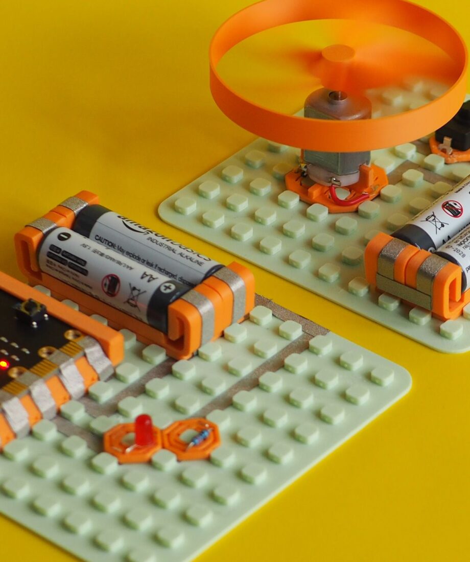 MakerTrack DC motor circuit on a modular grid board with AA battery mounts and conductive tape, shown with a spinning 3D printed fan attachment.