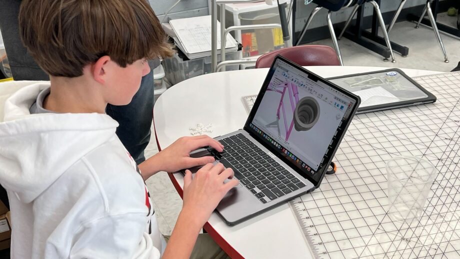 Student designing a 3D model using Autodesk Fusion on a laptop in a classroom