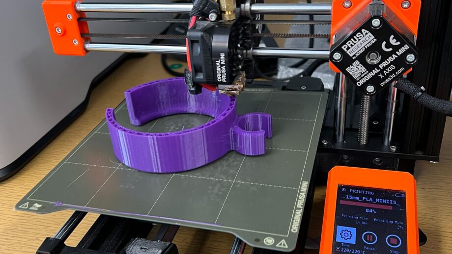3D printer creating a purple assistive device component on the build plate