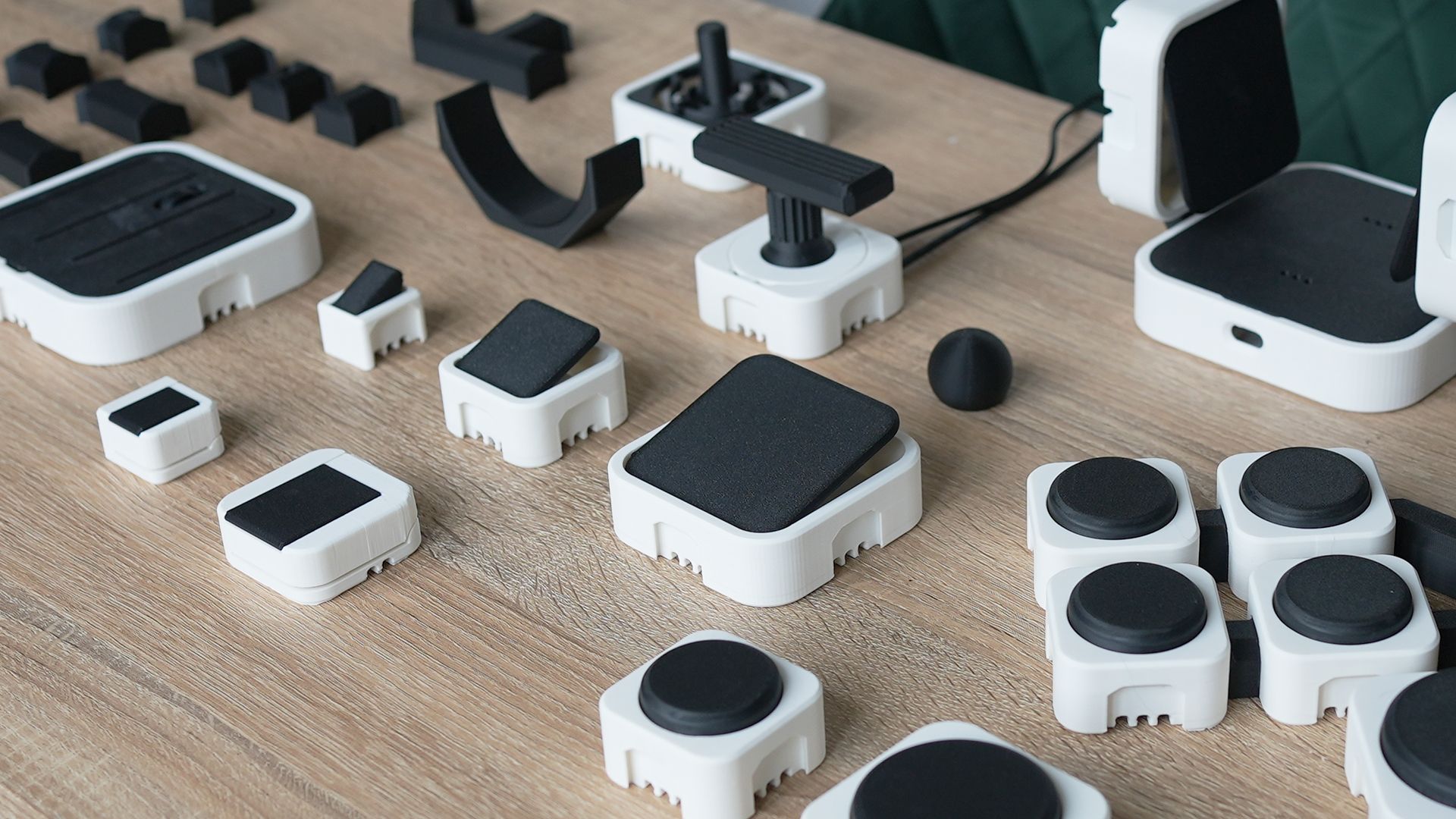 Collection of assembled PrintSwitch modules including assistive switches, joysticks, connectors and interface docks on a wooden table.