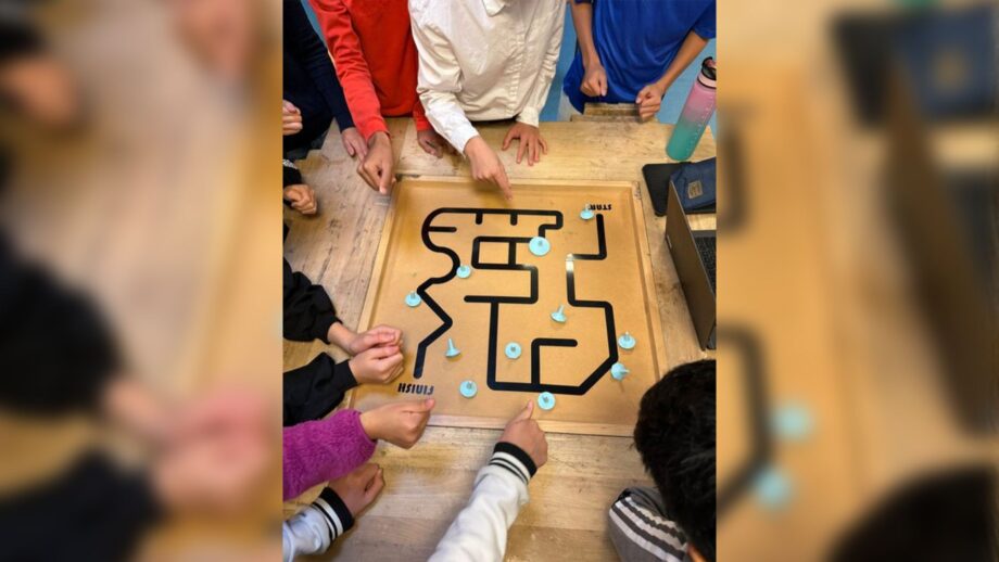 Students testing their 3D printed spinning tops on a wooden game board.