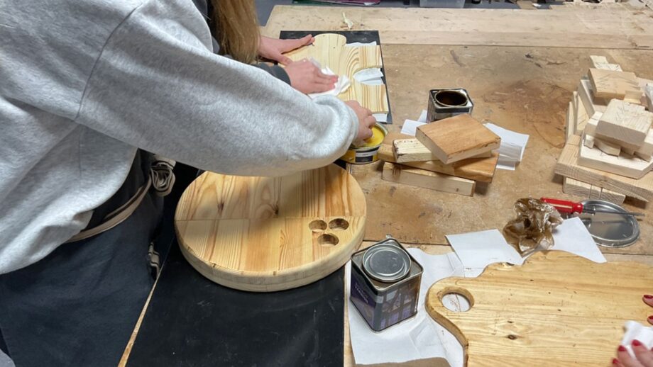 Students applying a finish to wooden charcuterie boards at a classroom workbench.