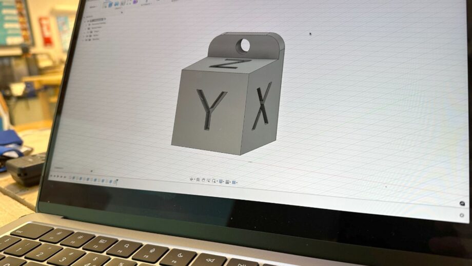 Laptop displaying a calibration cube keyring design with X, Y and Z markings in Autodesk Fusion.